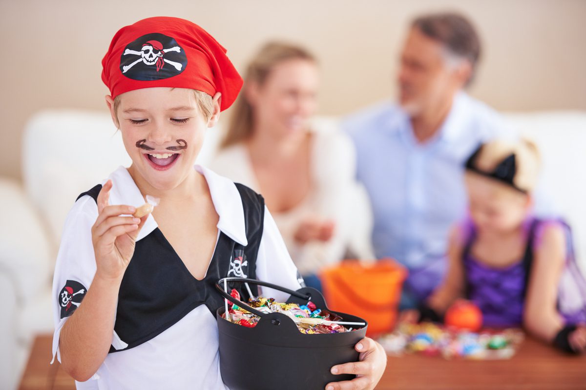 Young boy dressed as a pirate enjoying Halloween candy with his family in the background.