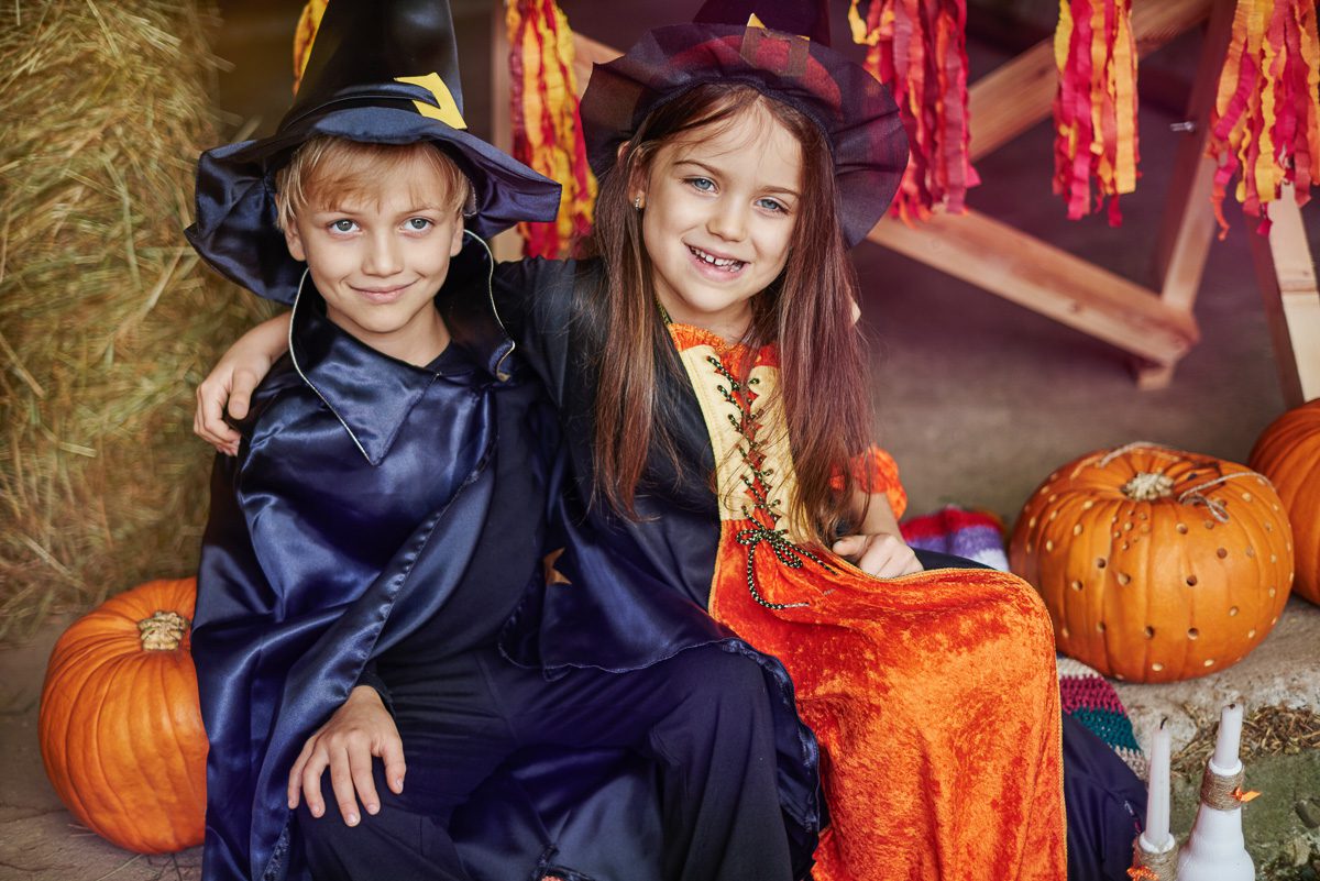 Children dressed in Halloween costumes surrounded by pumpkins and festive decorations.